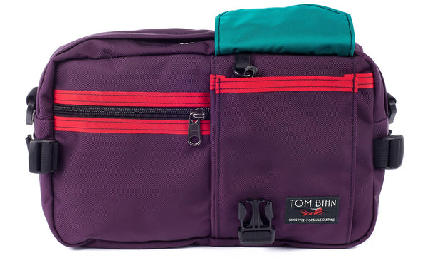 The LGD in Aubergine/Red/Viridian. Front view of the bag, buckle pocket lifted up showing the Viridian lining.